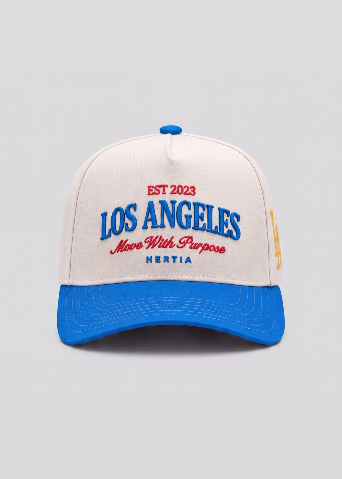 A structured baseball cap with an off-white crown and a bright blue curved brim. The front features embroidered text reading 'EST 2023 LOS ANGELES Move With Purpose NERTIA' in blue and red.