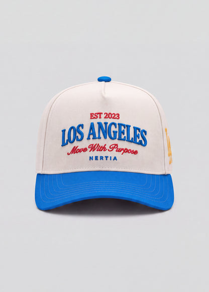 A structured baseball cap with an off-white crown and a bright blue curved brim. The front features embroidered text reading 'EST 2023 LOS ANGELES Move With Purpose NERTIA' in blue and red.