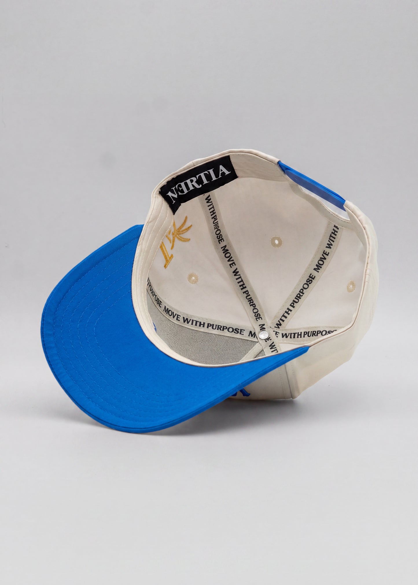 A structured snapback cap shown from the back, featuring a vibrant blue curved brim and a cream-colored crown. The inside of the crown is visible, showing a black brand label reading 'NERTIA' and a gold logo, along with white text on the suspension straps.