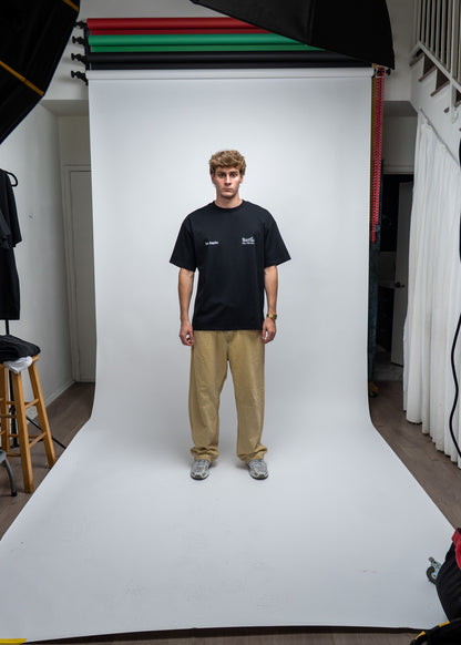 Person wearing a black t-shirt with visible branding on a white studio backdrop