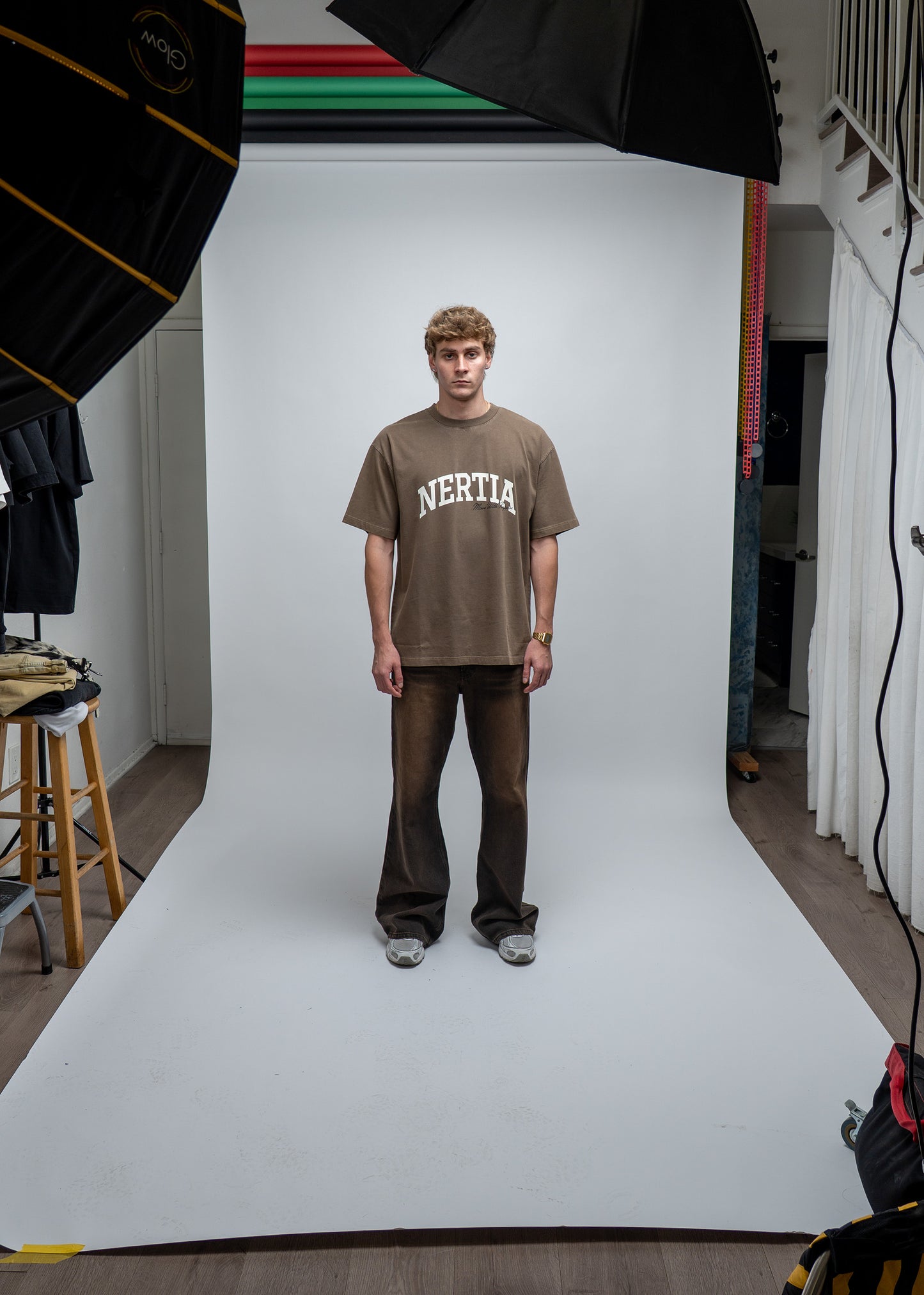 Person wearing a brown 'NERTIA' t-shirt standing in a studio setting with photography equipment.