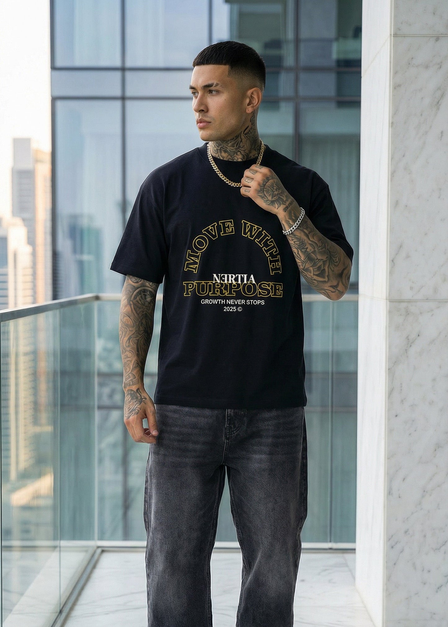Man wearing a black t-shirt with text and graphics, standing on a balcony with modern architectural background.
