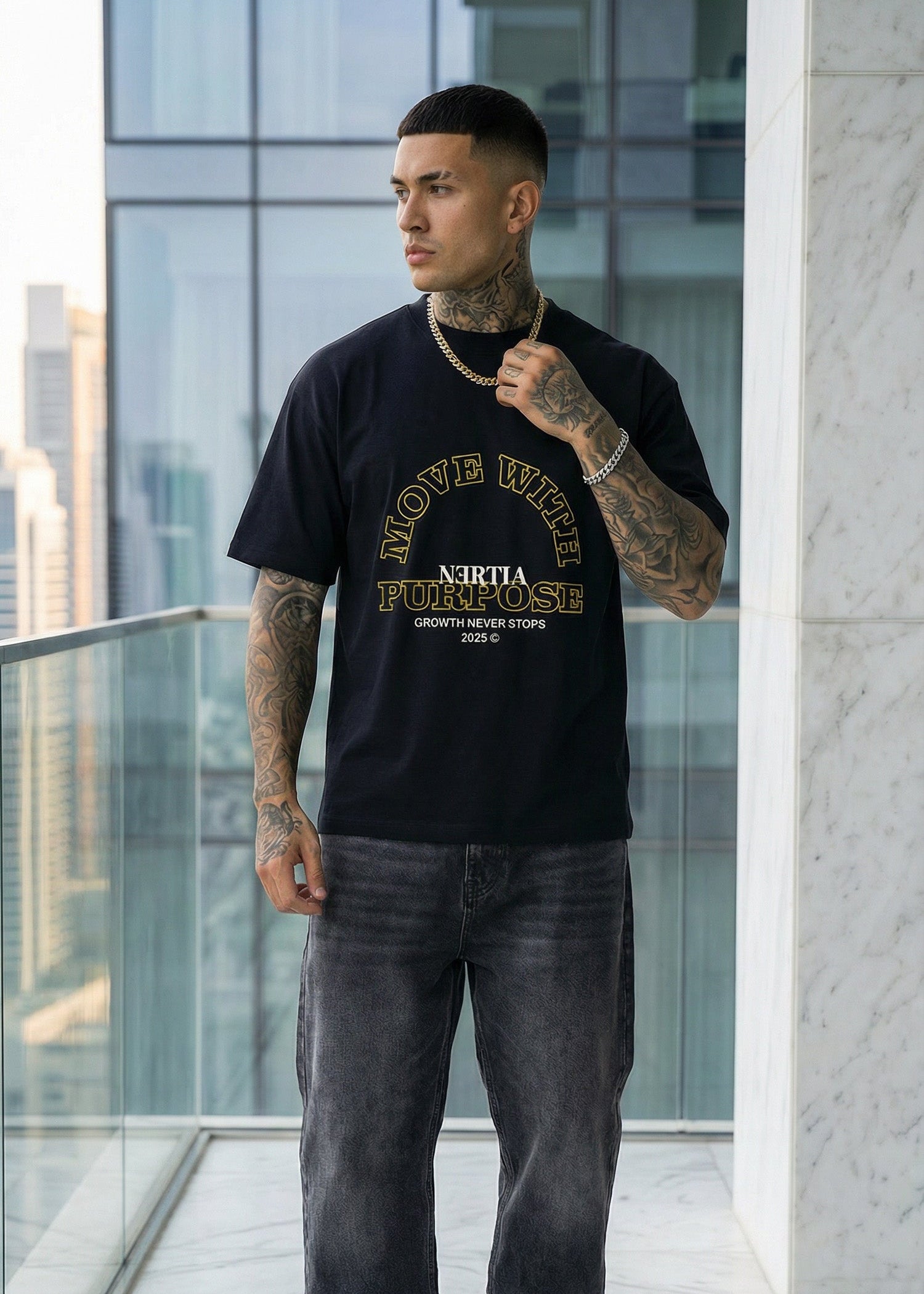 Man wearing a black t-shirt with text and graphics, standing on a balcony with modern architectural background.