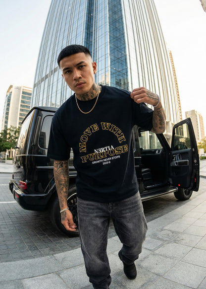 Man wearing a black t-shirt with text standing in front of a black SUV with open door in an urban setting.