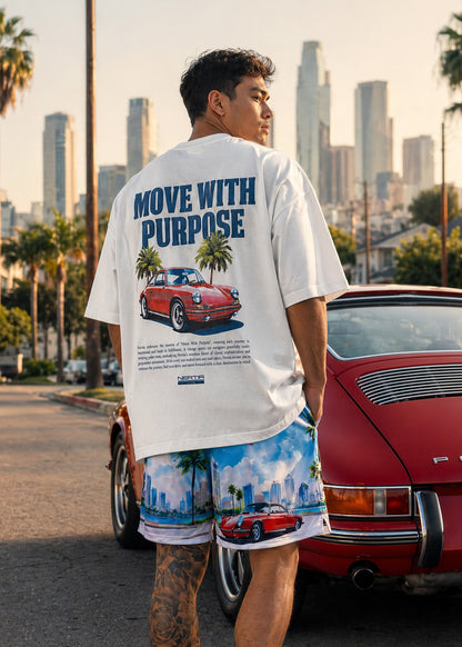Man wearing a white t-shirt with a graphic and text, standing in front of a red car with a cityscape in the background.