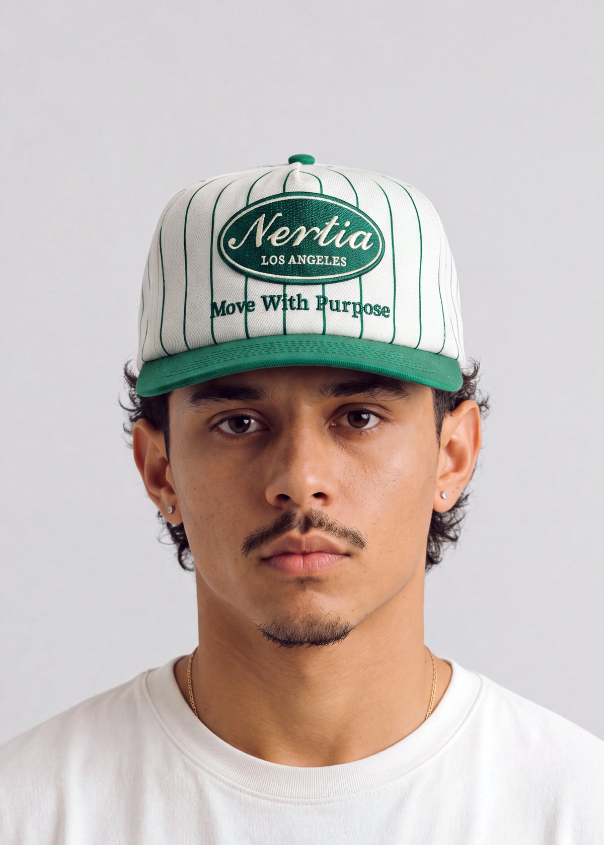A man wearing a white pinstripe baseball cap with green trim and a green front patch that reads 'Nertia Los Angeles' and 'Move With Purpose'.