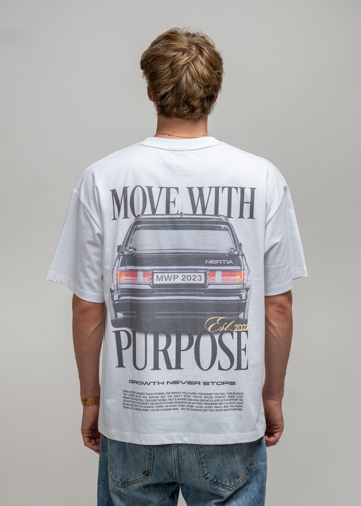 Person wearing a white t-shirt with a graphic and text on the back, standing against a plain background.