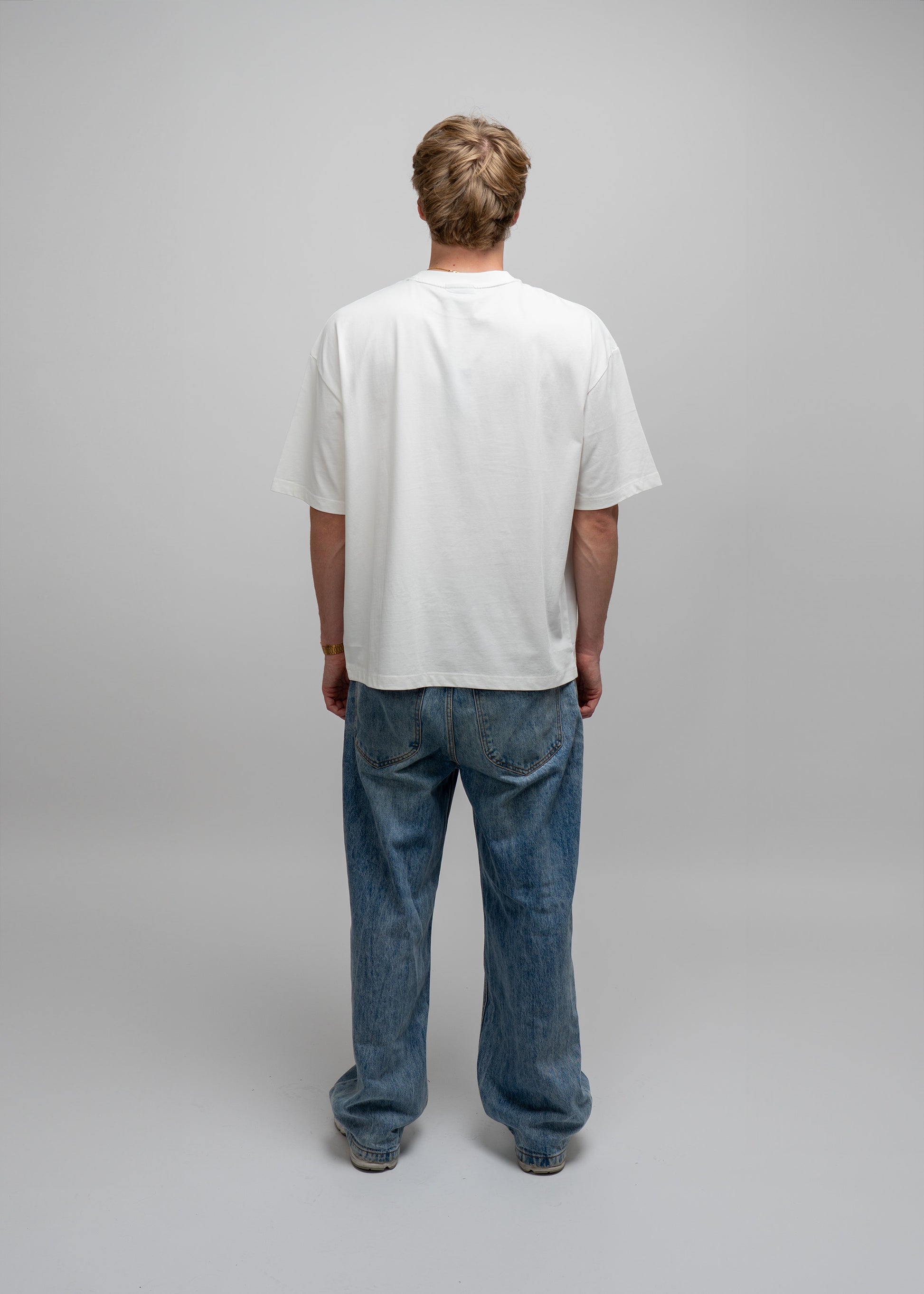 Person wearing a plain white t-shirt and blue jeans on a gray background