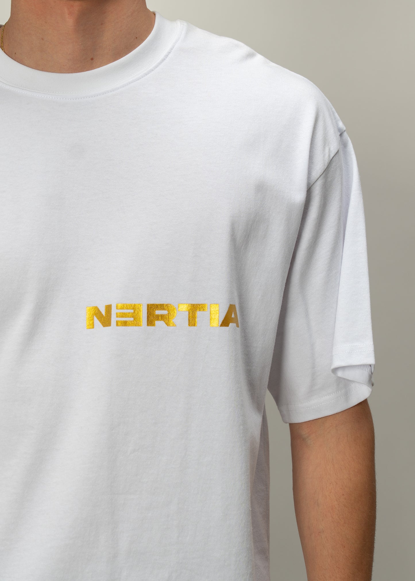 White t-shirt with gold 'NERTIA' logo worn by a person on a neutral background