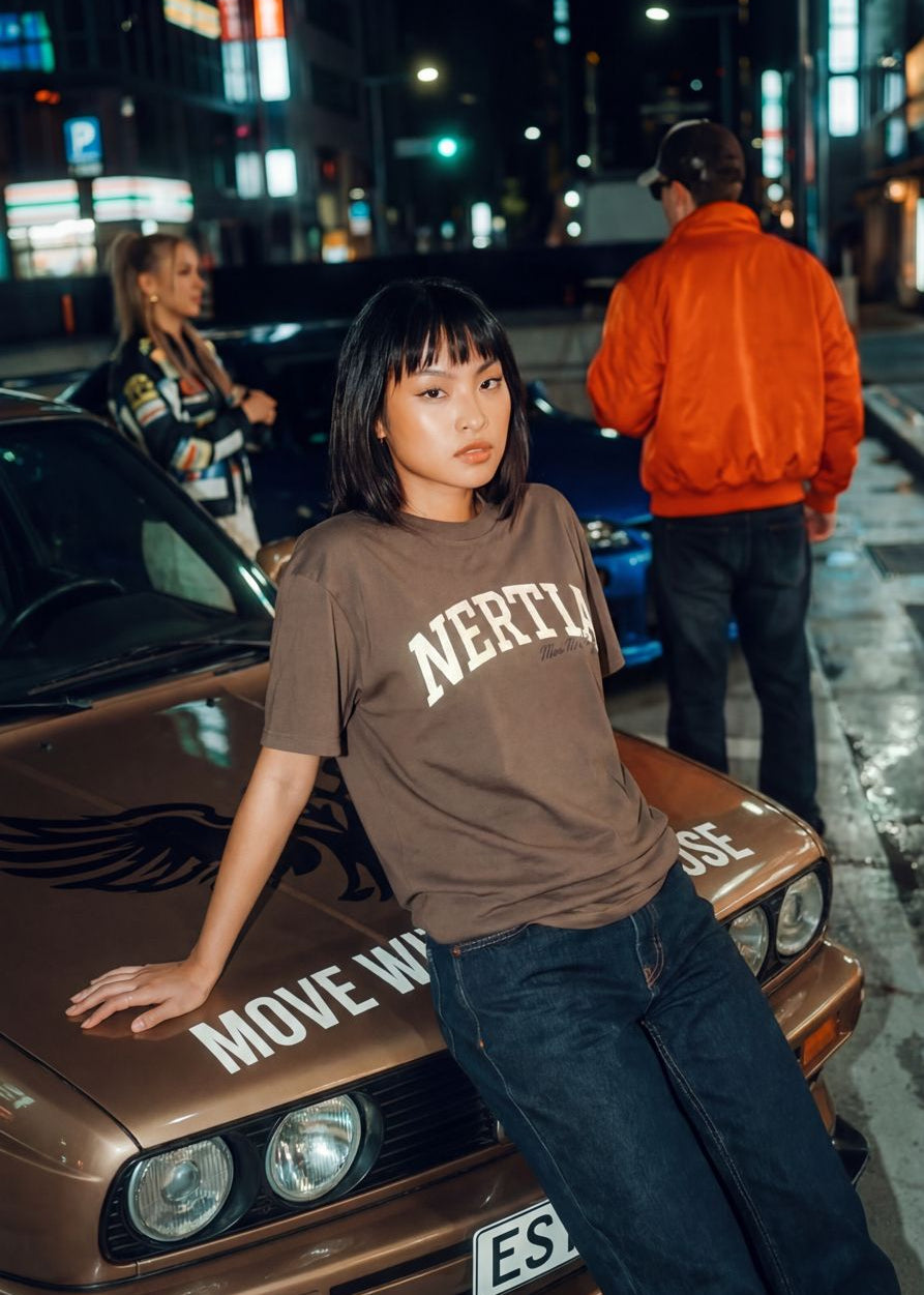 Person wearing a 'Nervio' shirt leaning against a car in an urban night setting