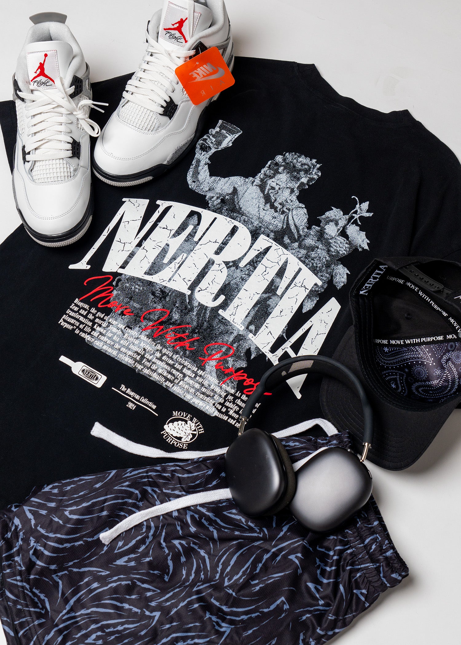 Black t-shirt with graphic design, white sneakers, and black headphones on a light gray background